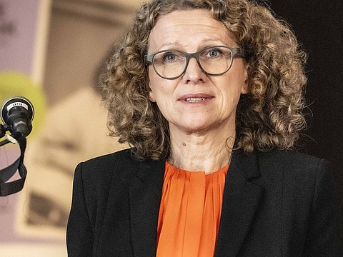 Auf dem Foto ist eine Frau, die an einem Rednerpult steht. 