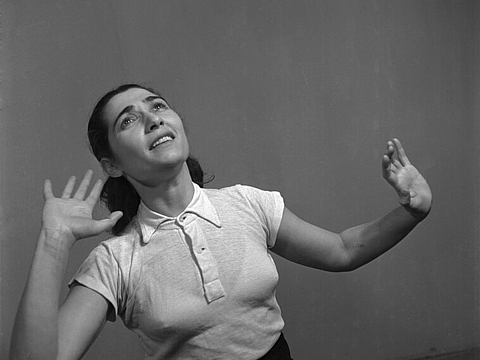 Eine Frau posiert mit theatralischem Gesichtsausdruck und erhobenen Händen in T-Shirt.