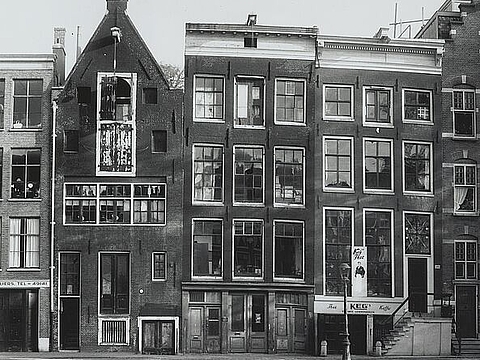 Frontansicht einer Reihe von schmalen Häusern, davor ein Kanal.