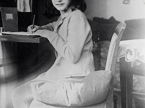 Eine Jugendliche sitzt an einem Schreibtisch und schaut in die Kamera, in der Hand hält sie einen Stift.