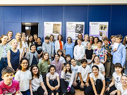 Auf dem Foto sind viele Kinder zu sehen, die sowohl hocken als auch stehen. In der Mitte in der letzten Reihe stehen vier Erwachsene Frauen zwischen den Kindern.