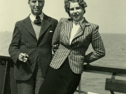 Ein Foto von einem Mann und einer Frau. Sie stehen nebeneinander an der Reling eines Schiffes. Im Hintergrund ist ein weites Gewässer zu sehen.
