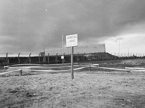 Ein Schild mit der Aufschrift »Grave Nr. 2« steht auf einer leeren, sandigen Fläche, im Hintergrund ein Zaun.