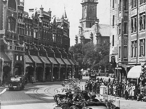 Ein Auto fährt durch die Straße einer Stadt, am Rand stehen viele Menschen.