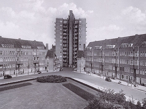 Platz mit Grünfläche, dahinter vierstöckige Wohnhäuser. Hochhaus im Hintergrund.