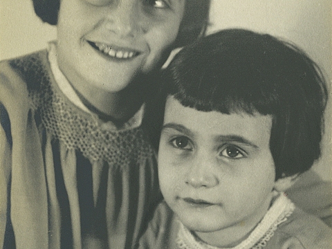 Die Gesichter von zwei nebeneinander sitzenden Mädchen. Sie lächeln und schauen an der Kamera vorbei.