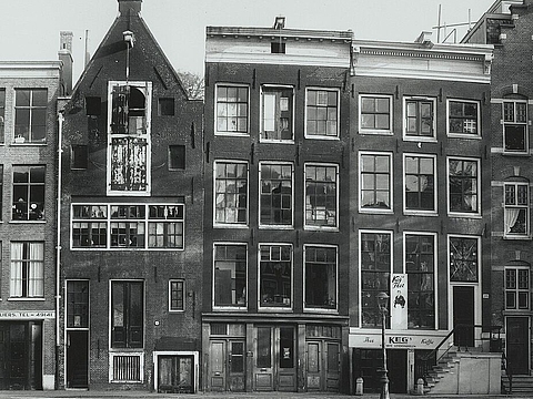 Ein Kanal, dahinter eine Reihe schmaler, dreistöckiger Gebäude mit großen Fenstern.