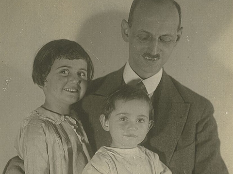 Studioaufnahme: Jüngeres und älteres Kind auf dem Schoß ihres Vaters, lächelnd.