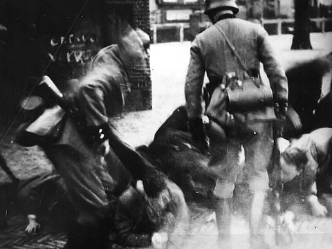 Zwei Soldaten beugen sich über mehrere am Boden liegende Personen.