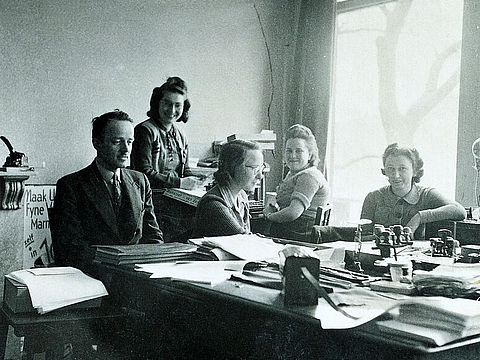 Fünf Erwachsene an Schreibtischen verteilt in einem Büro.